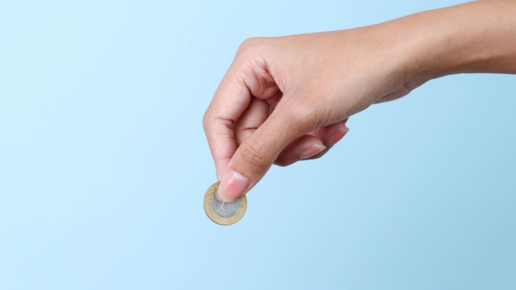 mão segurando uma moeda de um real em fundo azul