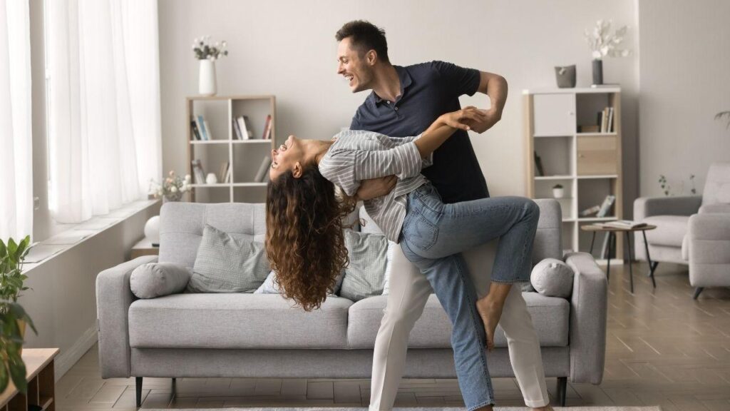 Homem abraçando a mulher numa sala de casa.
