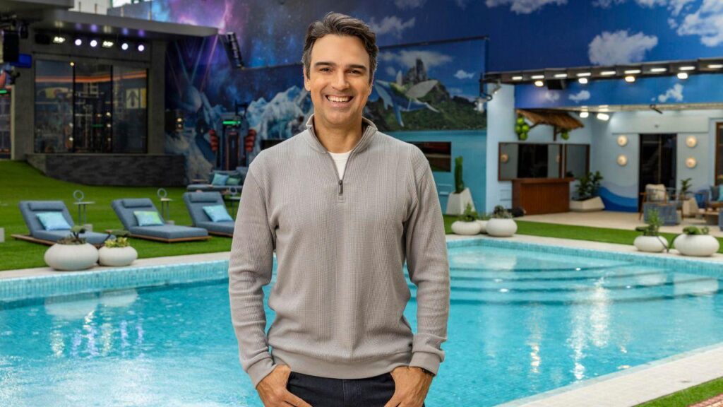 Tadeu Schimdt. Homem branco, cabelo castanho, camiseta preta sorrindo, ao fundo desfocado.