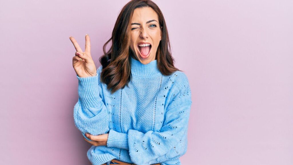 Mulher branca usando suéter azul num fundo rosa.