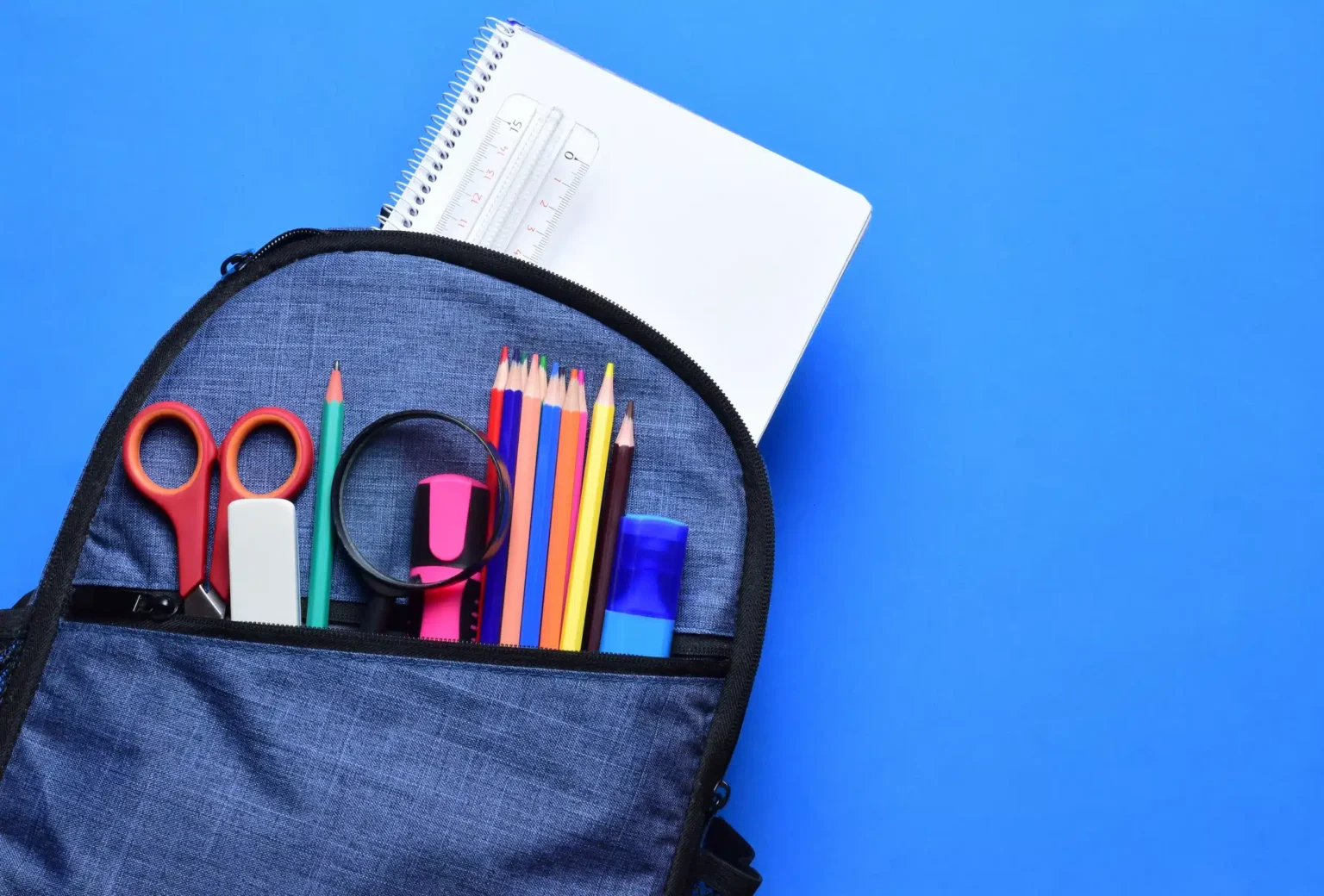 Mochila escolar com lápis de cor, tesoura, caderno e outros itens.